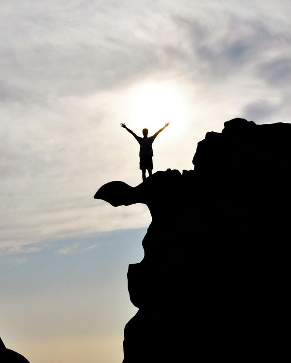 Silhouette of a person in a warrior yoga pose against a bright sky.